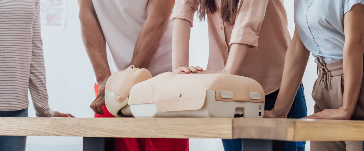 panoramic shot of group of people performing cpr on dummy during first aid training