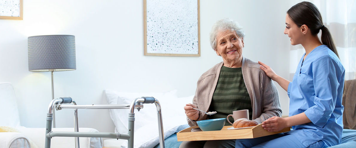 Care worker serving dinner for elderly woman on geriatric hospice