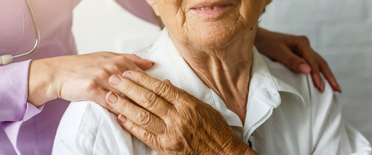 Elderly female hand holding hand of young caregiver at nursing home