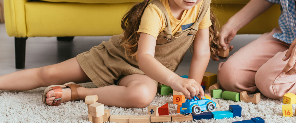 cropped view of babysitter near child playing with toy car