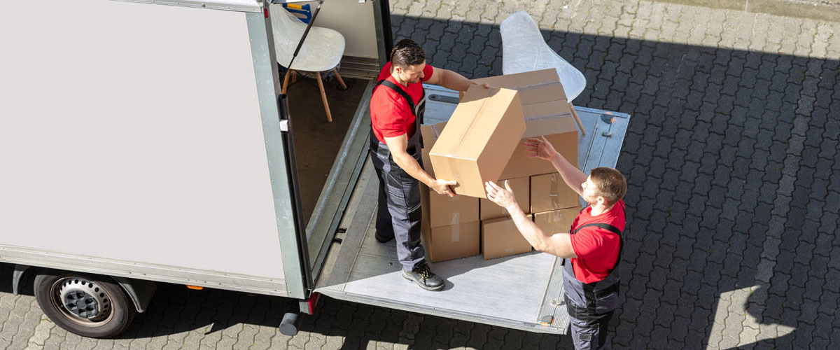 Male Movers Unloading The Cardboard Boxes Form Truck