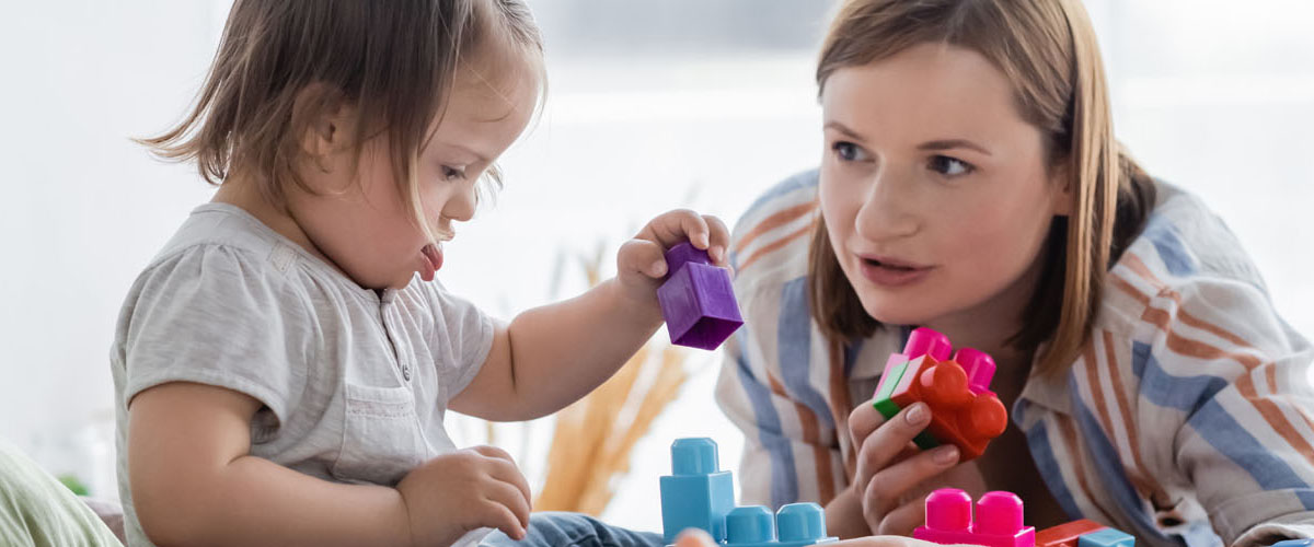 Mother talking to daughter with down syndrome playing building blocks at home