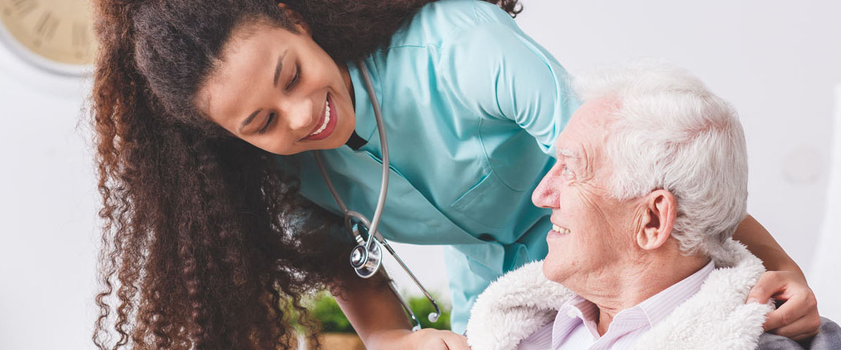 Panorama of a happy nurse with a stethoscope covering an elderly man with a blanket